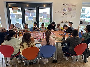 Gruppe von Kindern sitzen an einem großen Tisch und basteln
